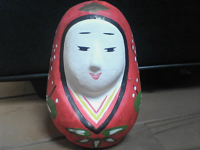 Bambola daruma femminile con volto bianco e abito rosso.