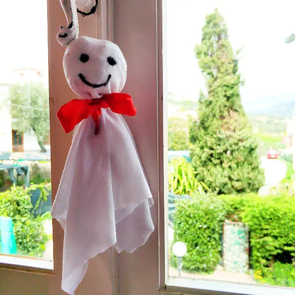 Teru teru bozu bianco con fiocco rosso appeso davanti a una finestra.